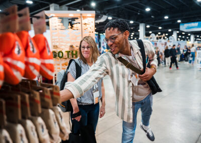 Credit: Keith Fearnow for Outdoor Retailer. Two attendees feeling hard good materials and smiling at Outdoor Retailer 2023.